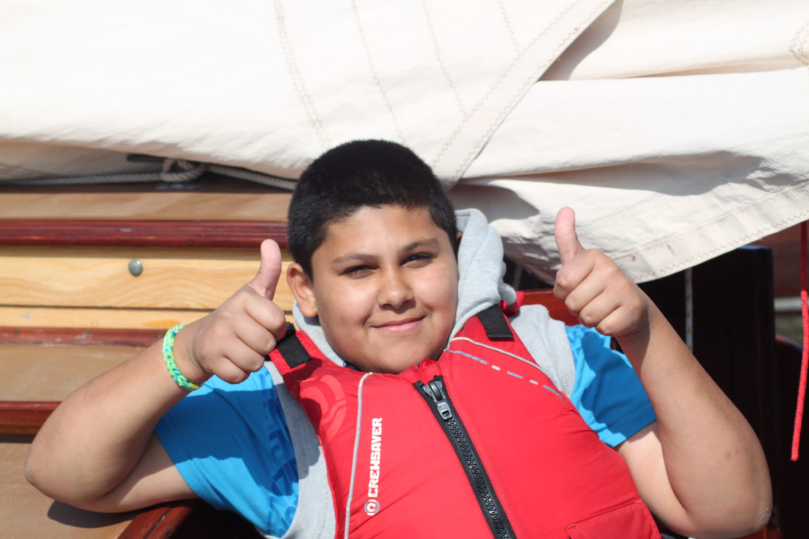 A smiling boy in a red buoyancy aid giving two thumbs up aboard a boat